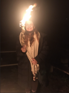 a person wearing a tallit smiles and holds up a lit homemade candle